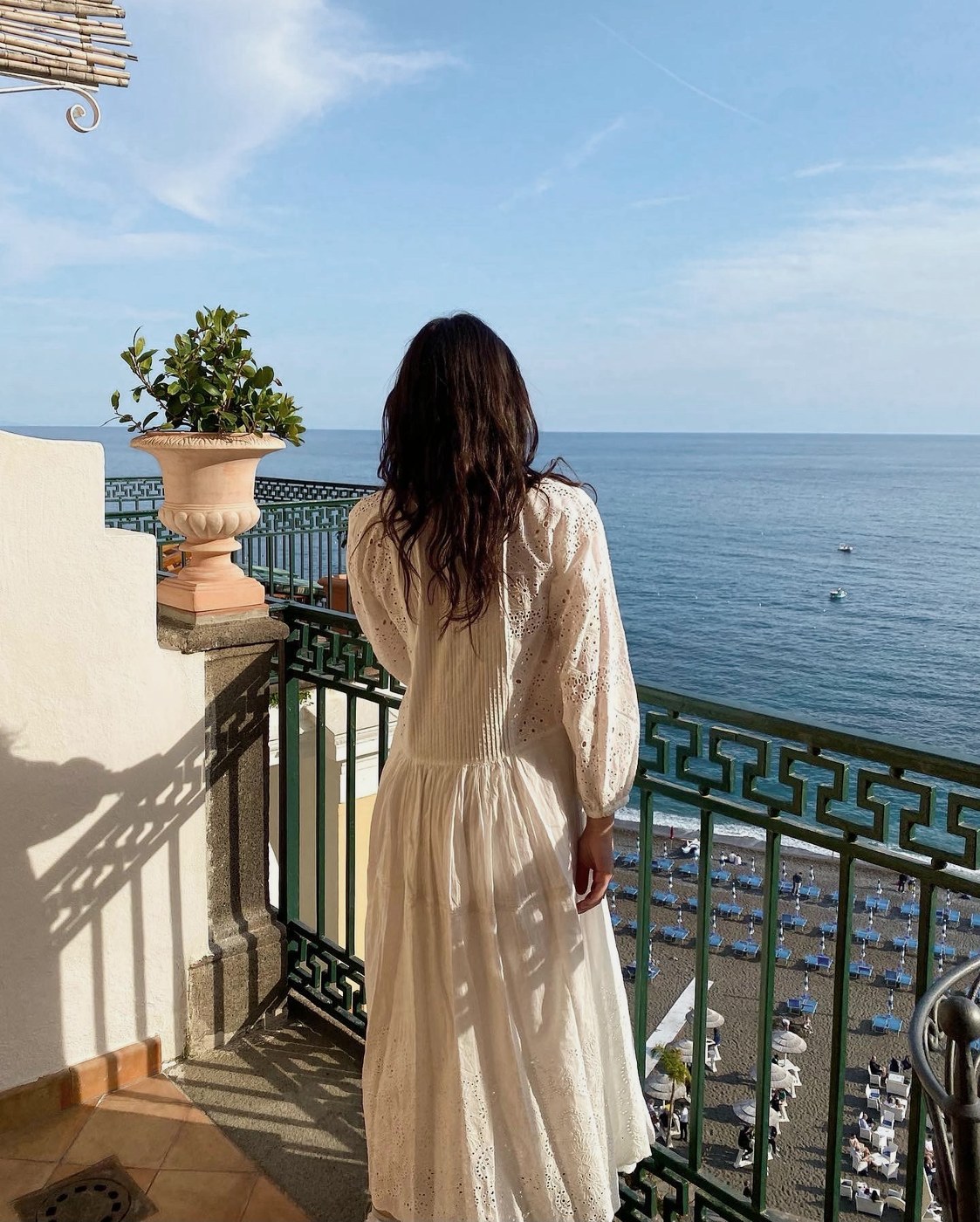 A guest in a white dress on a hotel balcony overlooking the sea and beach on the Amalfi Coast